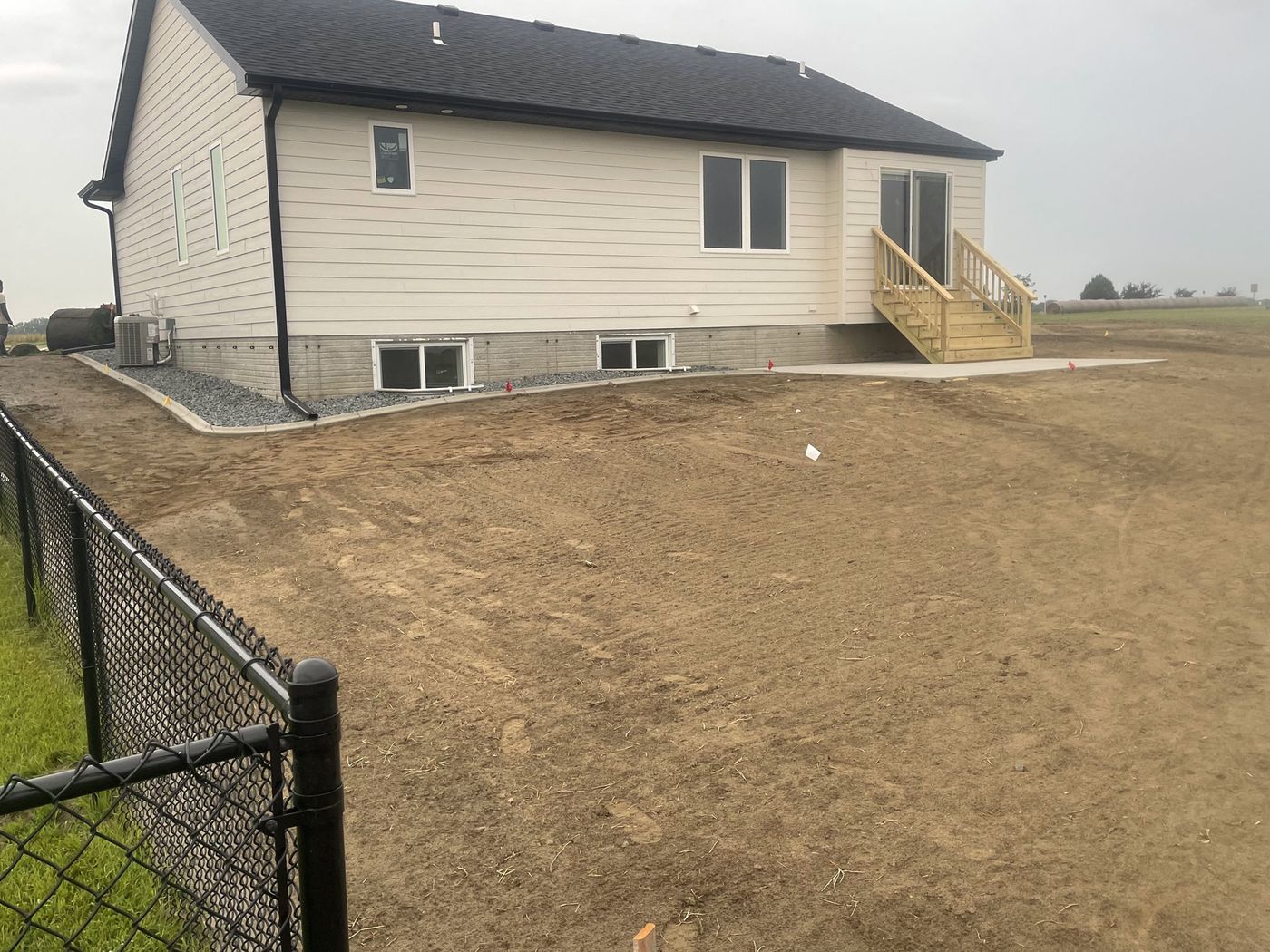 Residential backyard sod installation, before — bare graded dirt behind a new home